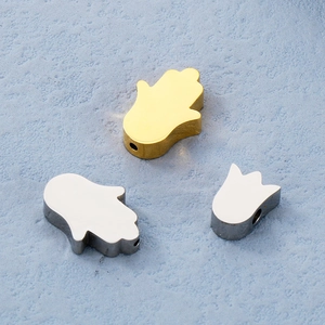Detailed view of metal Hamsa and tulip beads for DIY jewelry making on blue background