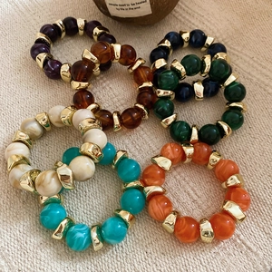 Macro shot of colorful acrylic beaded elastic rings with golden metallic spacers on fabric