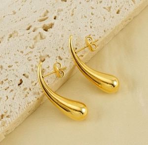Macro shot of gold teardrop earrings with high-polish mirror finish on textured stone