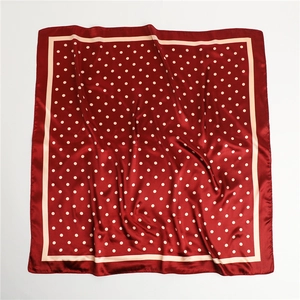 Detailed close-up of dark red polka dot silk scarf with elegant beige border accents