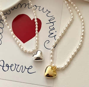 Detailed macro of gold and silver heart pendants on elegant freshwater pearl necklaces