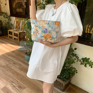 Floral fabric cosmetic pouch held by model in front of a cozy artistic cafe setting