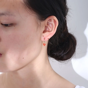 Close-up of a model wearing a red heart-shaped pendant earring with a golden hoop closure