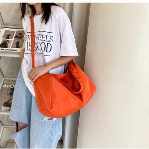 Side view of a bright orange large capacity oxford hobo bag worn by a model