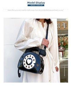 Detail of vintage black telephone crossbody bag with heart dial shown on a model