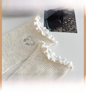 Detailed close-up of white knitted socks with ruffle cuffs and grey bow embroidery