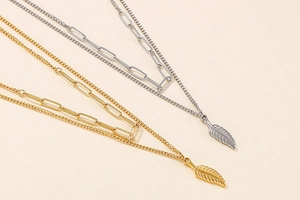 Detail view of double-layered paperclip necklaces with delicate feather pendants in gold and silver