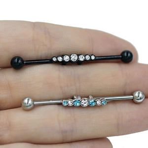 Gros plan de piercings industriel avec cristaux marquise tenus entre les doigts