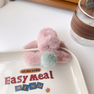 Detail of pink faux fur hair claw with mint green pompom on a ceramic plate