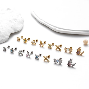 Detailed close-up of surgical steel ear studs with butterfly, cross and zircon accents