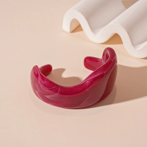 Detail view of deep magenta acrylic resin cuff with white marble texture on beige background