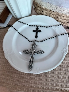 Close-up of gothic rhinestone hollow cross pendant and black bead necklace on vintage plate