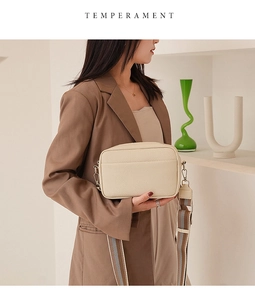 Detail of cream crossbody camera bag featuring lychee texture and striped woven strap