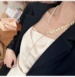 Dettaglio di una collana lunga a Y con foglia d'oro, perle e nappa su una modella