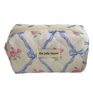 Quilted floral makeup bag with pink roses and blue ribbons on a soft off-white fabric