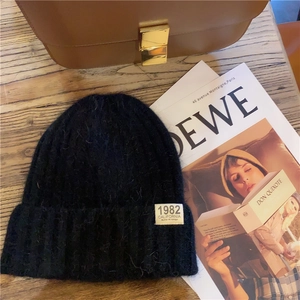 Flat lay of a black knit beanie with a 1982 California label on a rustic wooden table