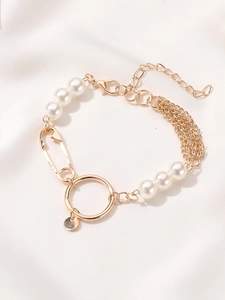 Detail of a golden paperclip bracelet with elegant white pearls on soft silk background