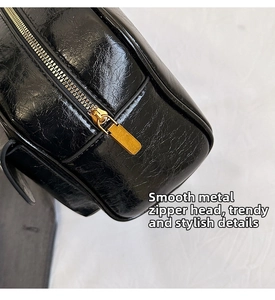 Close-up of black glossy leather messenger bag featuring a smooth gold zipper detail