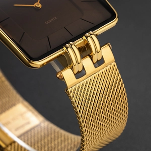 Macro shot of gold square watch case and black dial with metallic mesh strap detail