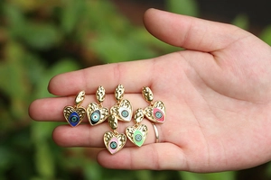 Detailed view of colorful enamel heart evil eye charms held in palm for size scale