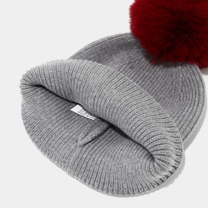 Detail of grey cable knit hat with a dark red faux fur pompom and 100% acrylic tag