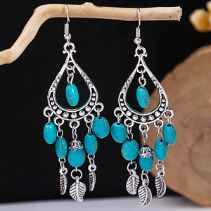 Detail of bohemian tassel earrings with turquoise beads and silver leaf charms on wood