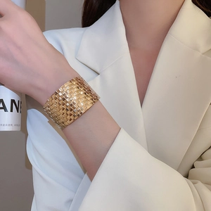 Close-up of golden wide cuff bracelet with woven metal texture on a model wearing a suit