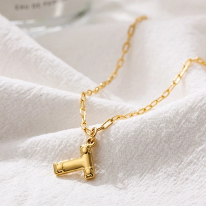 Close-up of golden bubble letter T pendant necklace on white fabric with perfume bottle