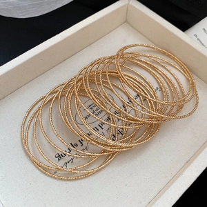Detail of stacked gold-toned bangles with hammered texture in a white jewelry box