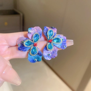 Detailed macro of flower-shaped earrings with blue-purple petals and crystal core