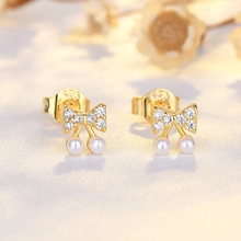 Close-up of gold bow earrings with sparkling zircons and dangling white pearls