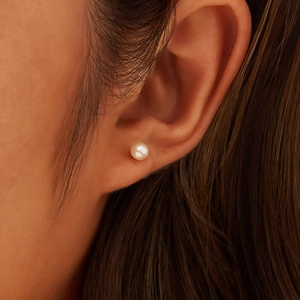 Close-up of a white natural freshwater pearl earring on a model's ear, classic style