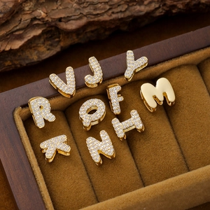 Gold plated bubble letter charms with pavé zirconia displayed in a wooden jewelry box