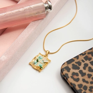 Detailed close-up of a vintage gold necklace with a green enamel butterfly picture frame pendant
