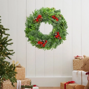 Christmas pine needle wreath with red berries and pine cones on a white wooden wall