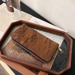 Vintage brown long zip-around wallet with pleated leather texture in a wooden tray