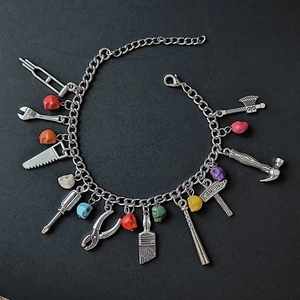 Détail d'un bracelet en chaîne argentée avec crânes colorés et pendentifs d'outils miniatures