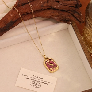 Macro view of gold stainless steel necklace with purple flamingo pendant on wooden tray