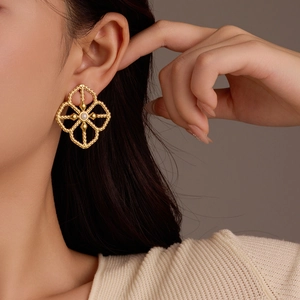 Gold hollow flower stud earrings with white pearl detail on model's ear