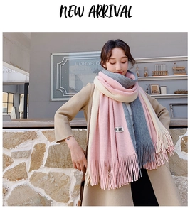 Detail of pink, grey, and cream knit scarf featuring thick fringe and a brand logo tag