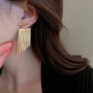 Close-up of golden long tassel drop earrings worn by a model with metal chain details
