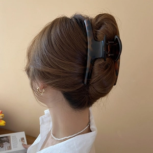 Large tortoiseshell hair claw clip securing a low bun on brunette hair in back view