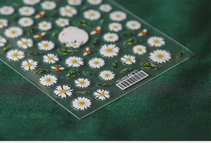 Macro shot of 3D daisy nail stickers with white petals, bees and green leaves on dark fabric