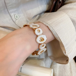 Close-up of golden irregular enamel拼接 elastic bracelet worn on wrist with beige shirt