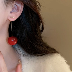 Detailed close-up of a model wearing a cherry drop earring with a red ball and gold stem