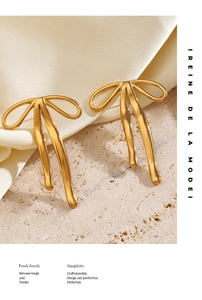 Dettaglio di orecchini a fiocco placcati oro 18K con design a nastro su seta color crema