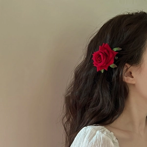 French vintage style red fabric rose hair clip with green leaves worn on brunette hair