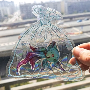 Detail of a rainbow prism suncatcher sticker showing goldfish pattern held in hand