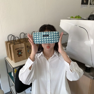 Gros plan d'une trousse en tissu à carreaux bleus et blancs tenue par un mannequin