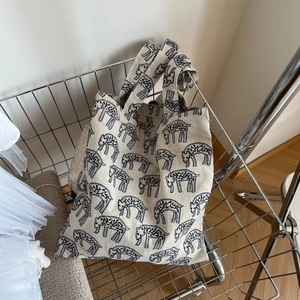 Minimalist beige canvas tote bag with black zebra embroidery on a metal cart